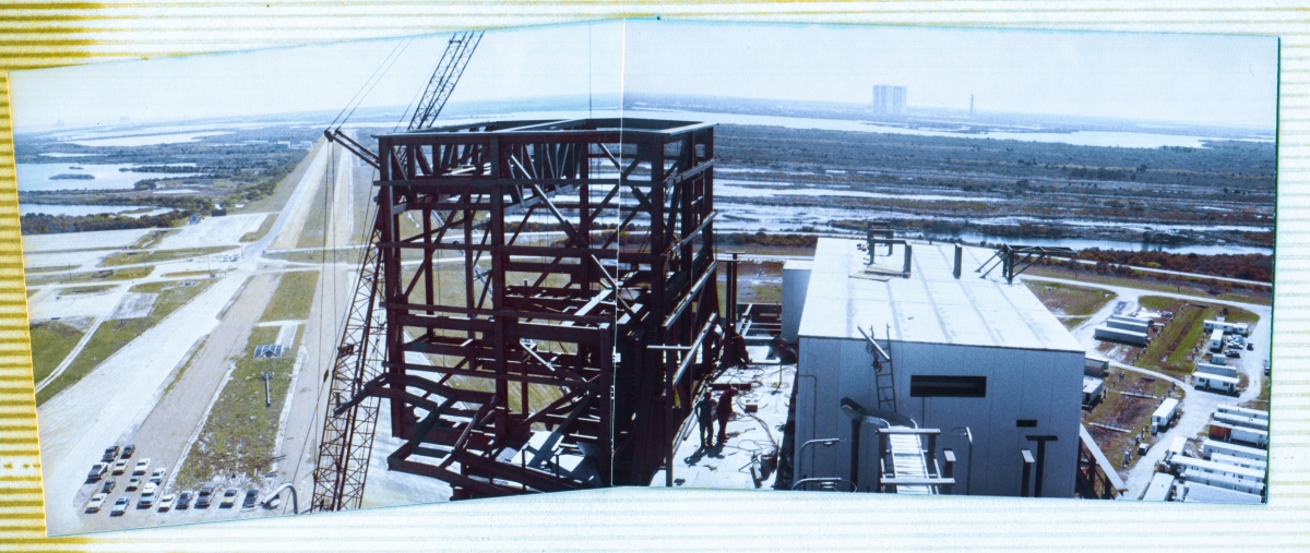 Image 009. Viewed from the south side of the 240-foot elevation of the Fixed Service Structure at Space Shuttle Launch Complex 39-B, Kennedy Space Center, this panorama encompasses a nearly ninety-degree field of view, and contains, from left to right, the far-distant SMAB and VIB of the Titan III Integrate-Transfer-Launch area just above the horizon, the Crawlerway extending southwards away from the launch pad, the skeletal steel framework of the RCS Room which sits on top of the Rotating Service Structure, the Hoist Equipment Room covered in white insulated-metal wall paneling with the VAB in the far distance on the horizon above it, and to the right of the VAB, the last remaining Apollo-era Launch Umbilical Tower, and in the lower-right area of the frame, the contractor field-trailers where the work of building the RSS was managed. Surrounding it all, the vast and brutally-unforgiving wetland wilderness of the Merritt Island National Wildlife Refuge. Photo by James MacLaren.